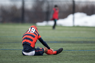 Syracuse defender Miles Robinson sits on the turf with his jersey tucked over his head.